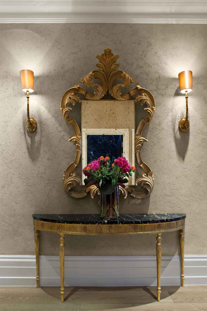 Pitted plaster walls, gilded classic mirror, marble and gold consul table, entrance hall design