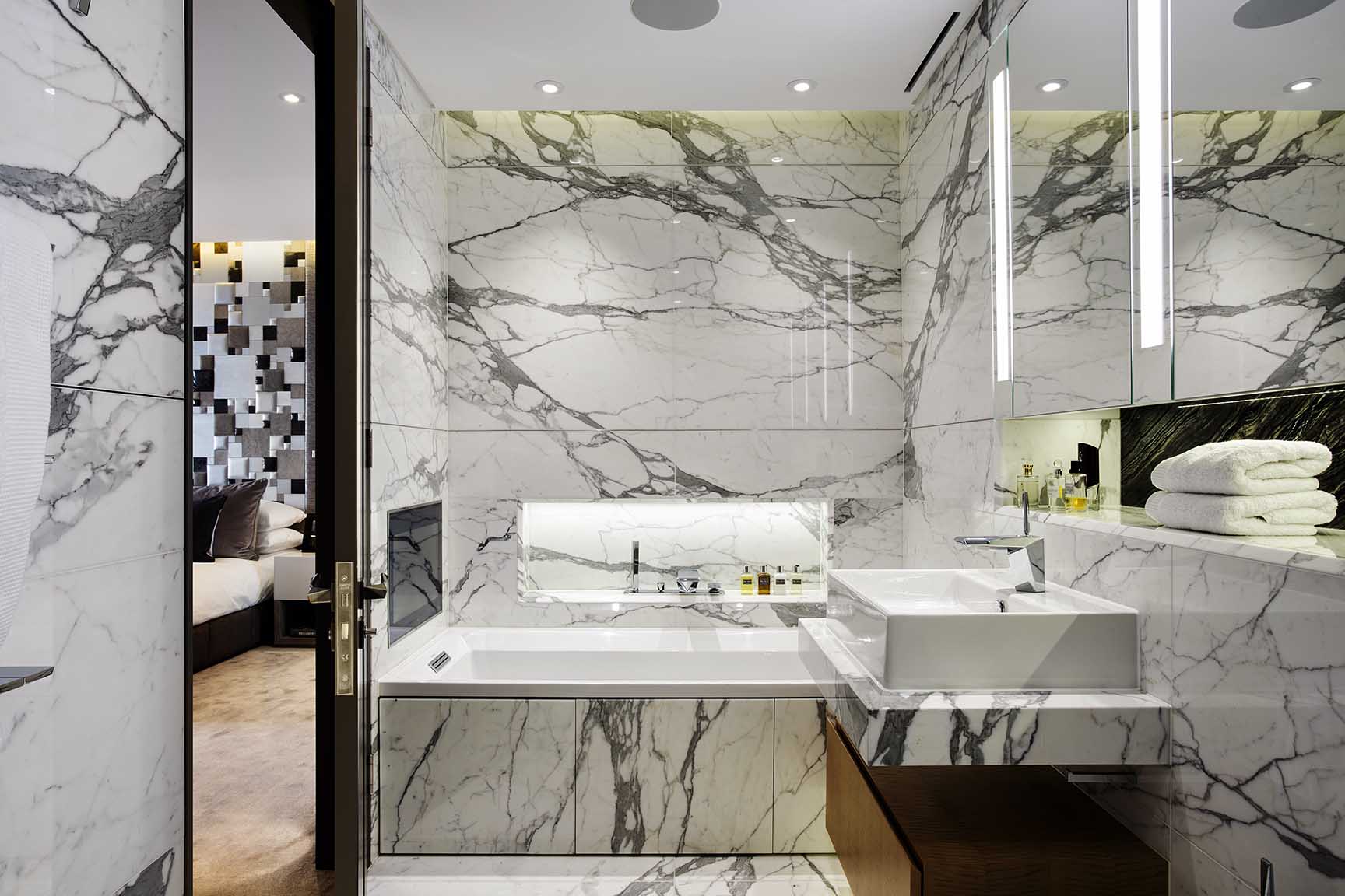 Bathroom clad in full height arabescatto marble slabs, integrated TV and ceiling speakers